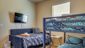 A room with a bunk bed, a single bed, a television mounted on the wall, a small table, and a window with blinds. - Las Cruces Oasis: Patio, Hot Tub + Mtn Views (Las Cruces)
