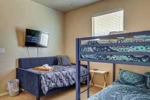 Una stanza con un letto a castello, un letto singolo, una televisione a muro, un tavolino e una finestra con persiane.