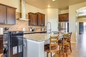 A kitchen with a central island, bar stools, a refrigerator, and wooden cabinets. - Las Cruces Oasis: Patio, Hot Tub + Mtn Views (Las Cruces)