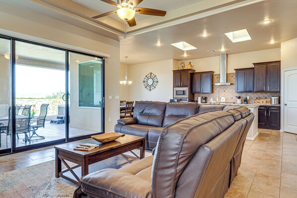 A spacious living area with a leather sofa, a dining table, and a kitchen with dark cabinets and a stainless steel range hood. - Las Cruces Oasis: Patio, Hot Tub + Mtn Views (Las Cruces)