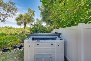 Ein Whirlpool mit Holzverkleidung, umgeben von einem weißen Zaun und üppigem Grün.