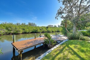 A wooden dock extending into a calm body of water, surrounded by lush greenery and a clear blue sky. - Private Hot Tub & Dock! Hutchinson Island Retreat (Fort Pierce)