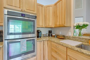A kitchen with two stainless steel ovens, wooden cabinets, a granite countertop, and a coffee maker. - Private Hot Tub & Dock! Hutchinson Island Retreat (Fort Pierce)