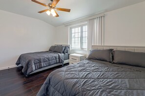 Ein Schlafzimmer mit zwei Betten, einem Deckenventilator, einem Fenster mit Vorhängen und einem Nachttisch.