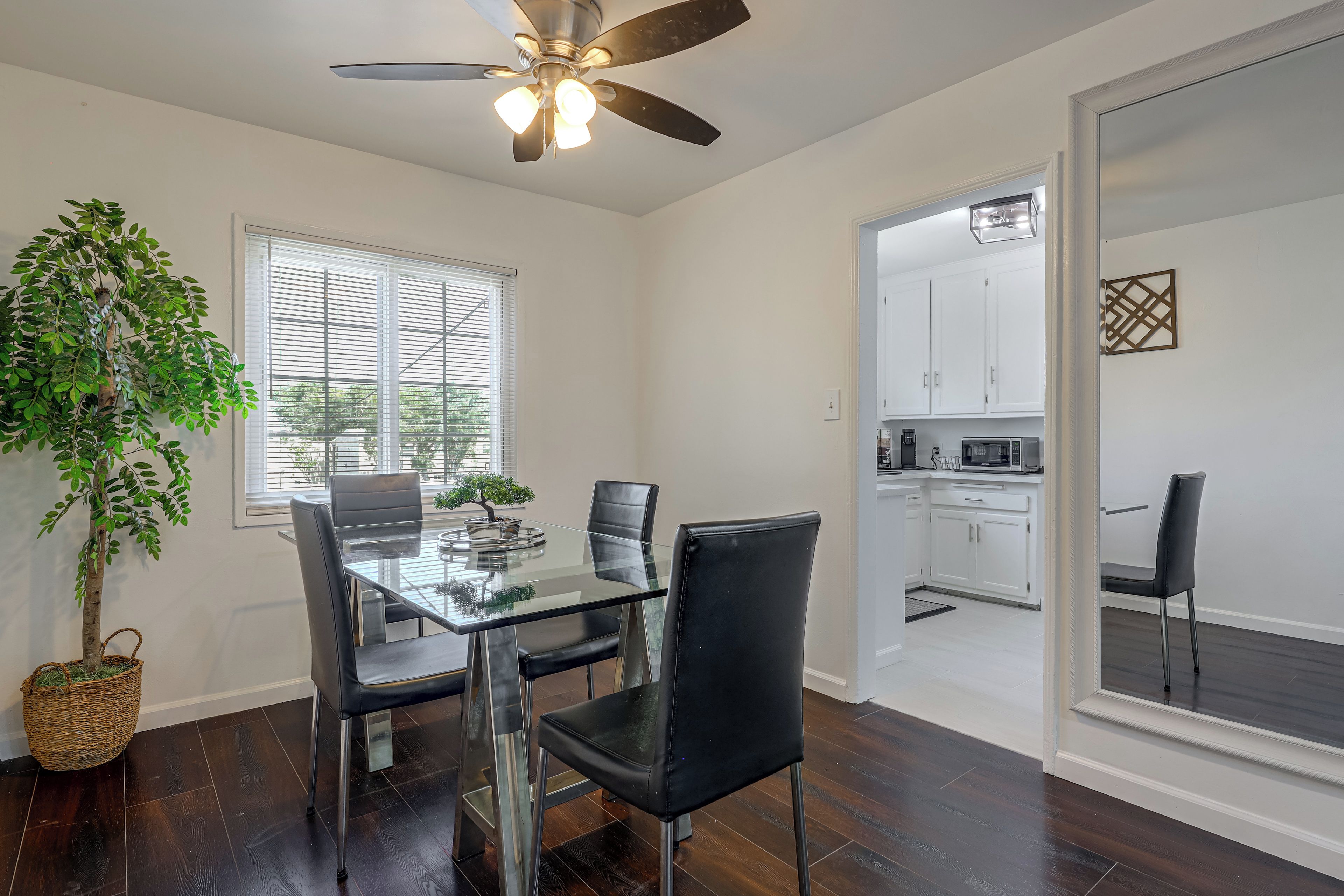 A dining area with a glass table, black chairs, a ceiling fan, and a view into a kitchen.