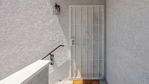 Uma porta branca com grades de metal, uma pequena luminária externa e uma fechadura de metal.