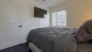 Quarto com cama, ventilador de teto, televisão fixada na parede e janela com persianas.