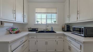 A kitchen with white cabinets, a window with blinds, a sink, a microwave, and a coffee maker.