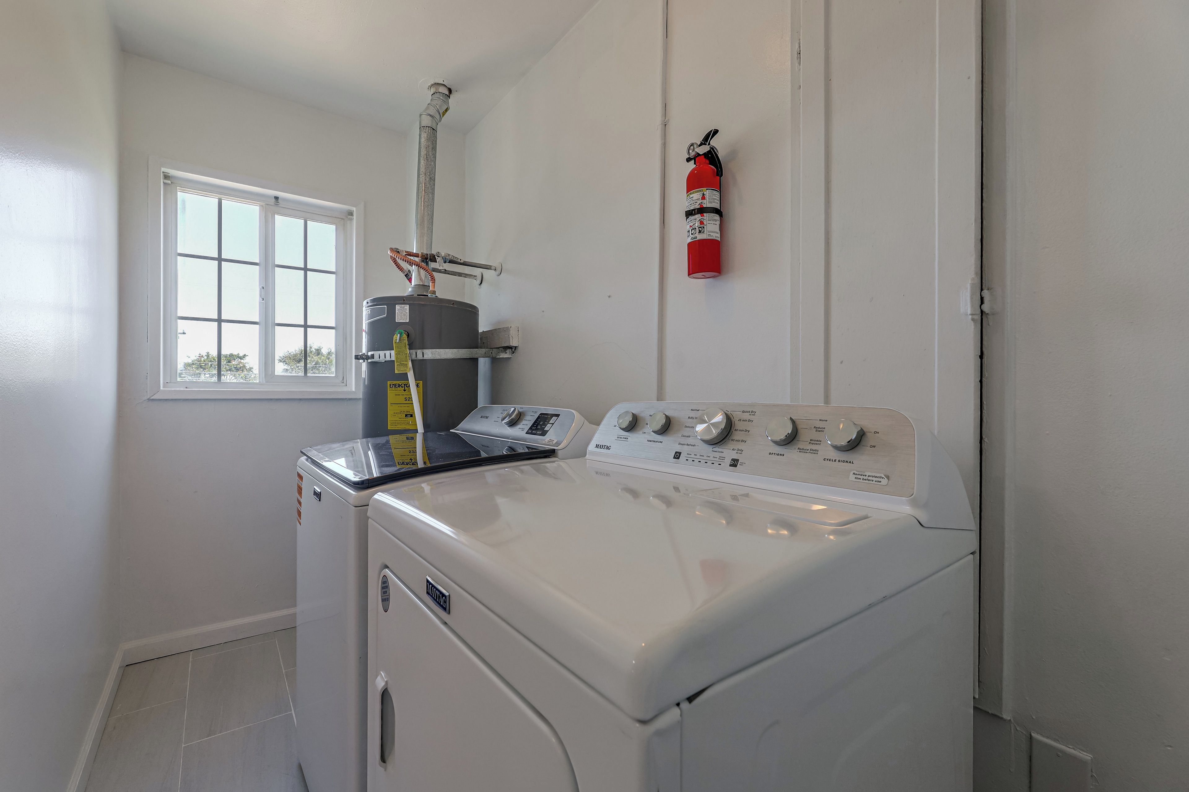 A laundry room with a front-loading washer and dryer, a window, and a fire extinguisher mounted on the wall.