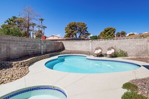 A swimming pool with a curved design, surrounded by a low stone wall and a paved deck.