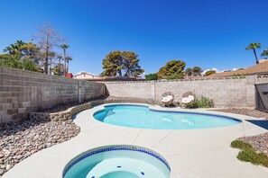 A swimming pool with a tiled edge, surrounded by a stone wall and a paved deck.