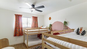 A room with two bunk beds, a ceiling fan, a window with curtains, a wall-mounted plant, and a patterned rug.