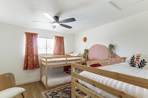A room with two bunk beds, a ceiling fan, a window with curtains, a wall-mounted plant, and a patterned rug.