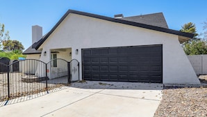 A single-story house with a garage, a gated driveway, and a concrete sidewalk.