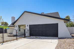 A single-story house with a garage, a gated driveway, and a concrete sidewalk.