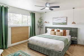 A bedroom with a bed, a ceiling fan, a window with blinds, and a painting on the wall.