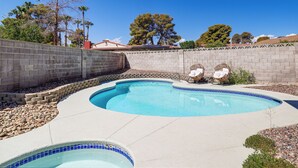 A swimming pool with a curved design, surrounded by a low stone wall and a paved deck.