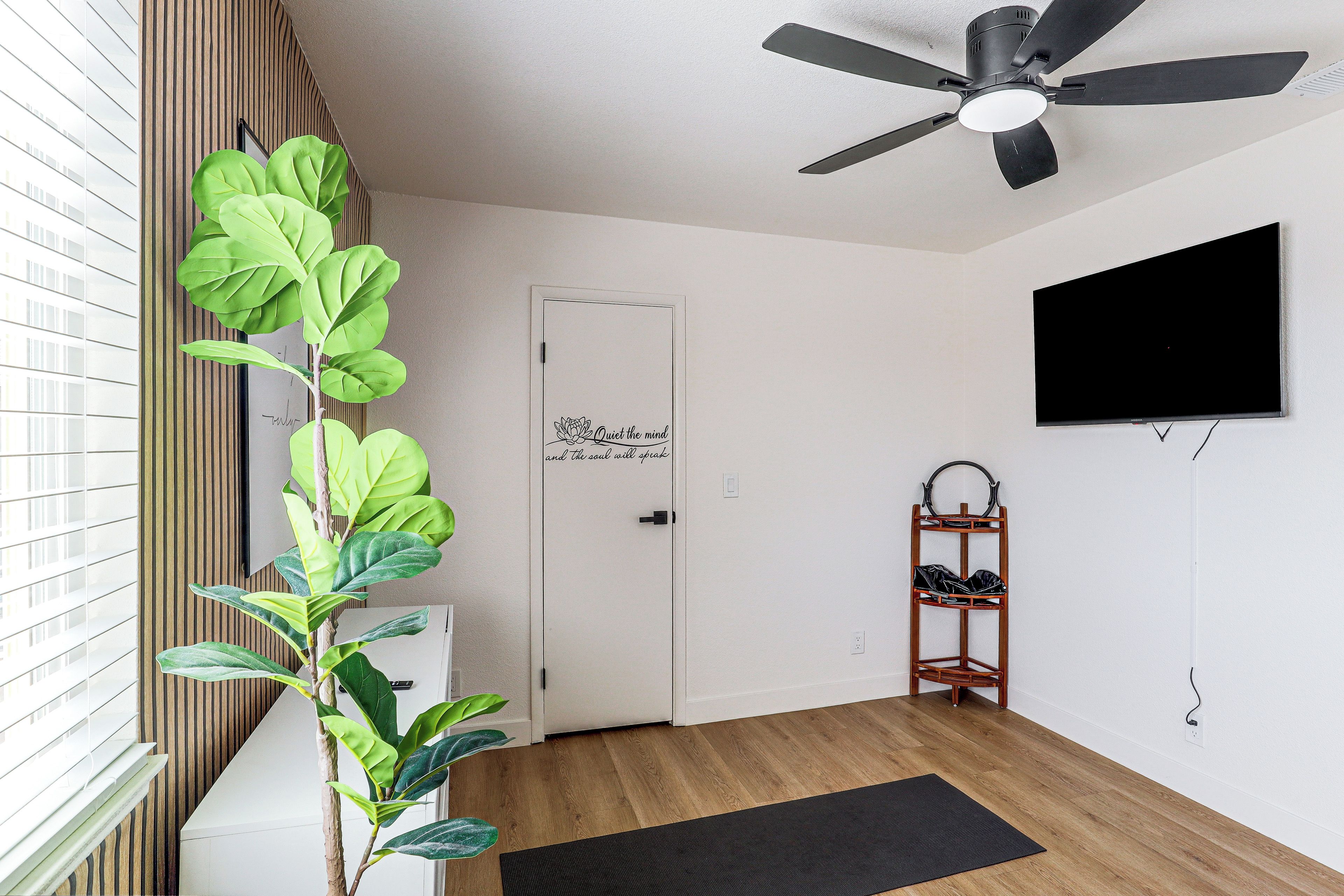 Una habitació amb ventilador de sostre, una porta amb el rètol 'Quiet the mind', un prestatge per a sabates i una televisió penjada a la paret.