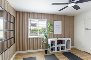 A room with a ceiling fan, a window with blinds, a potted plant, a framed quote on the wall, and a shoe storage unit.