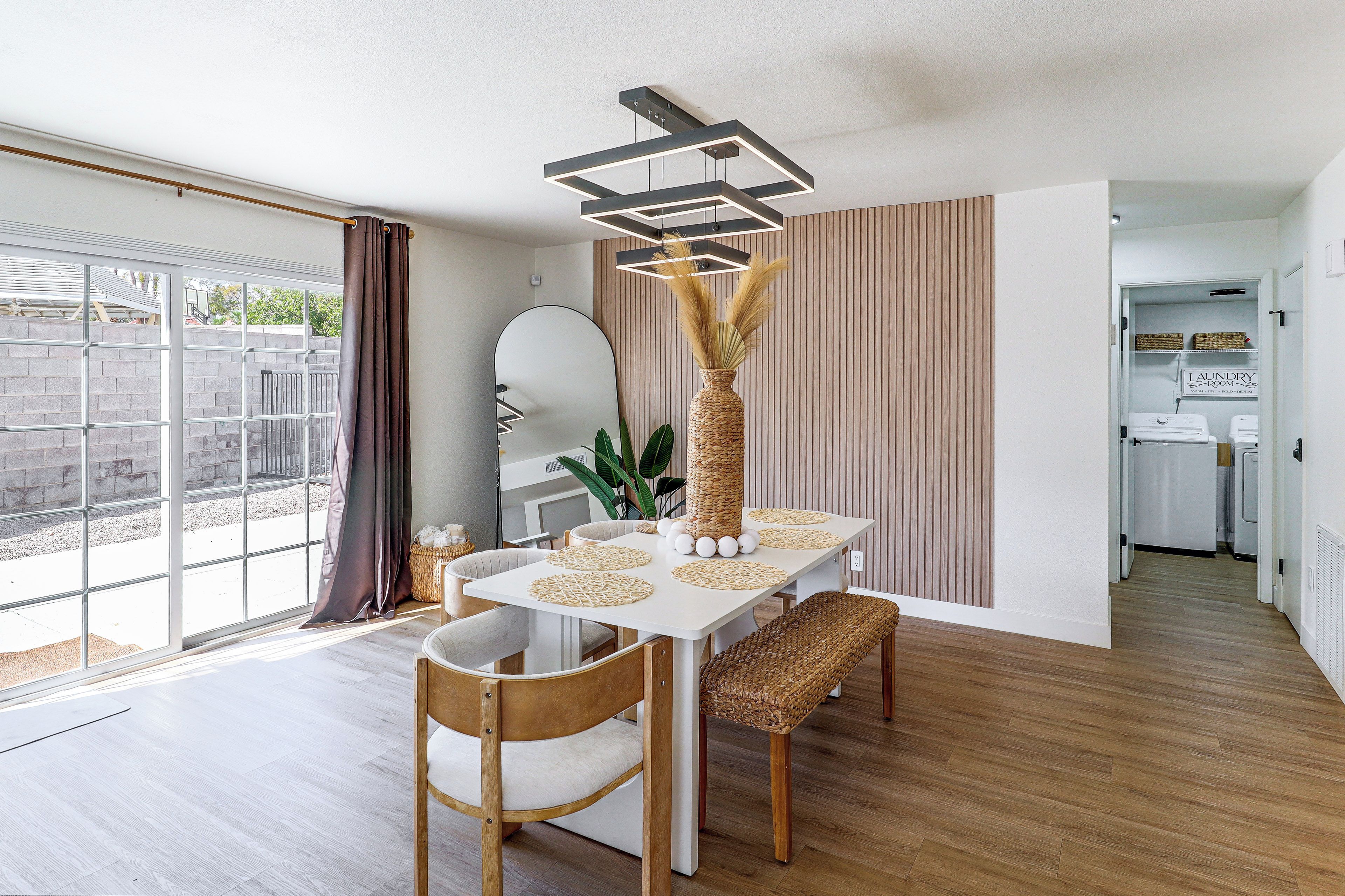 A dining area with a white table, woven chairs, a decorative vase, and a modern pendant light.
