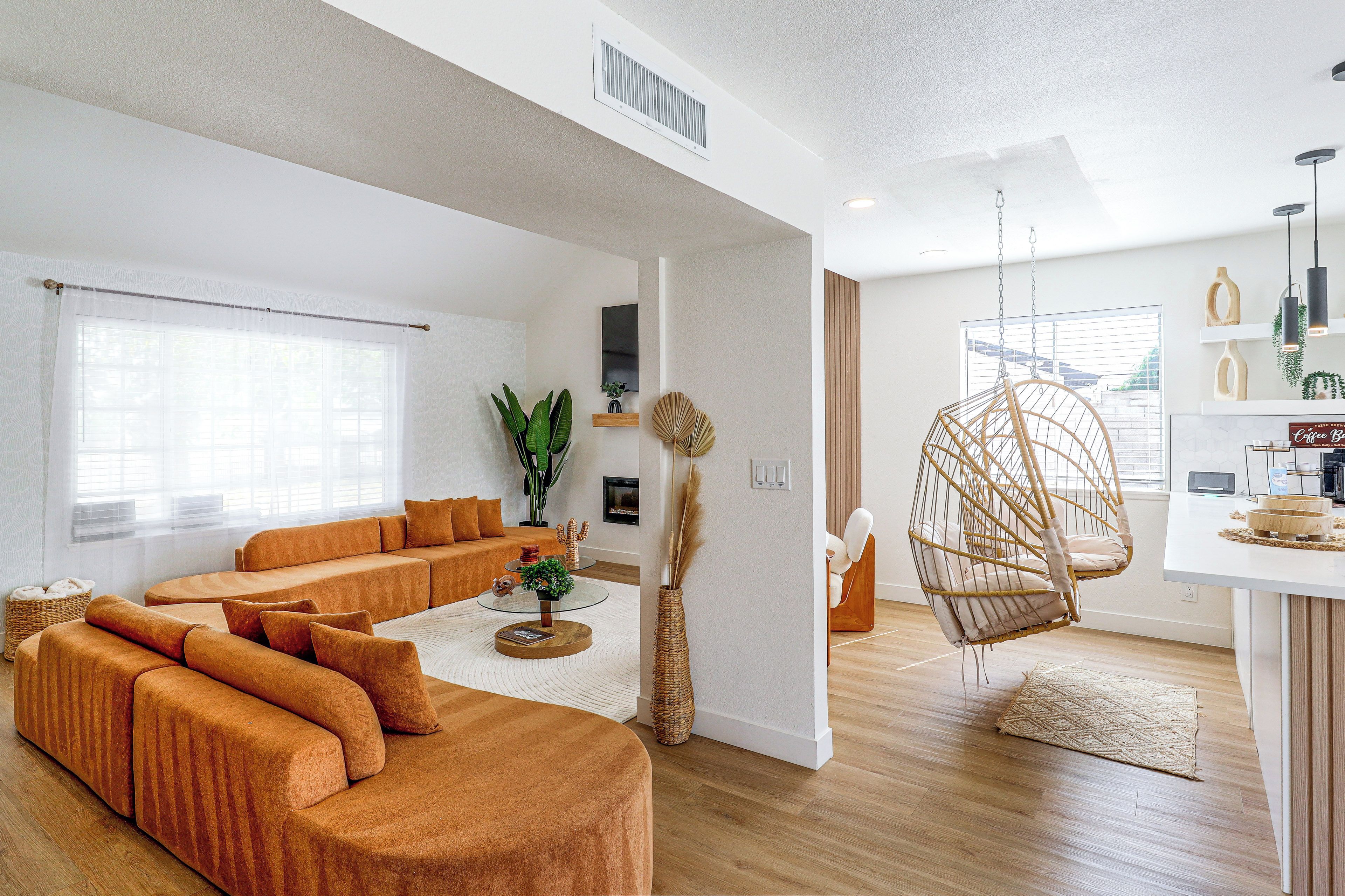 A modern living room with a sectional sofa, a hanging chair, and a coffee bar area.