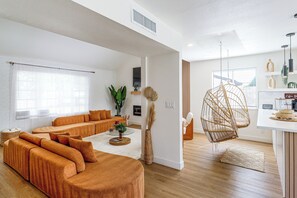A modern living room with a sectional sofa, a hanging chair, and a coffee bar area.
