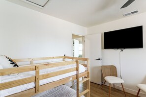 A room with a bunk bed, a chair, a flat-screen TV mounted on the wall, and a ceiling vent.