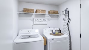 A laundry room with two white washing machines, a sign above them, and a shelf with baskets.