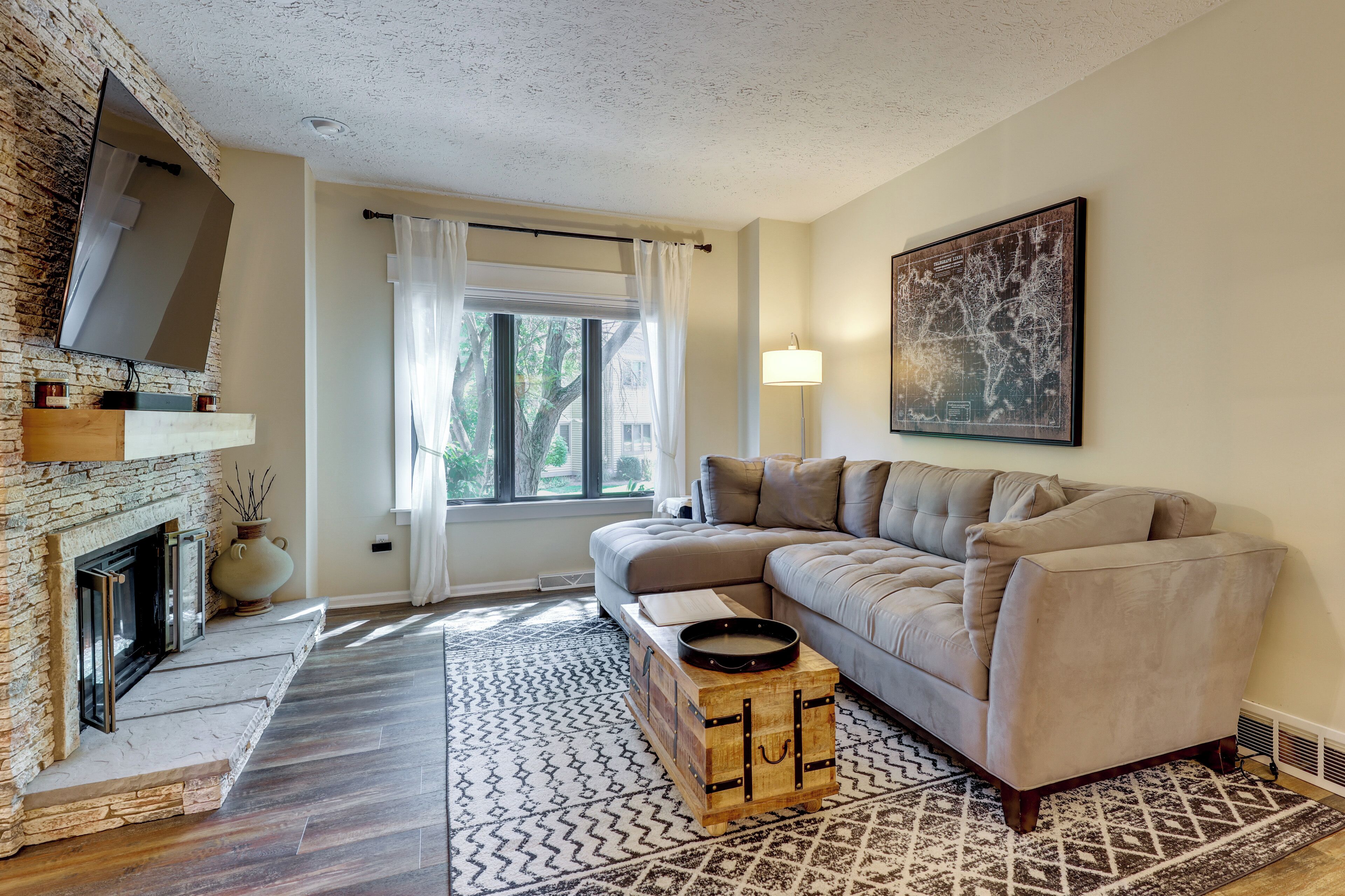 A modern living room with a fireplace, a sectional sofa, a patterned rug, and a large wall map.