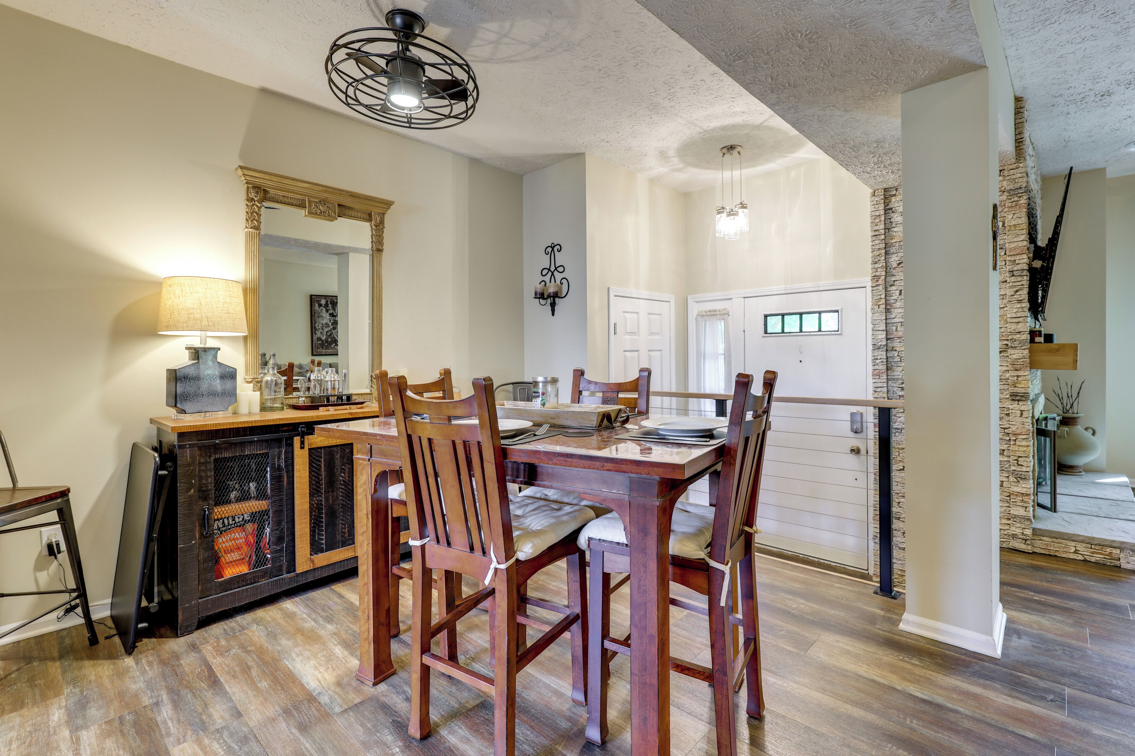 A dining area with a wooden table and chairs, a chandelier, and a kitchen in the background.