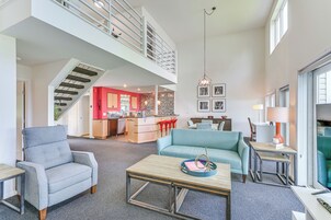 Un espacio habitable amplio con techo alto, una escalera que conduce a un nivel superior, una cocina con detalles rojos y un comedor con sofá azul.