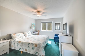 Une chambre à coucher comprenant un lit, un bureau, une chaise, une commode, un ventilateur de plafond et une fenêtre.