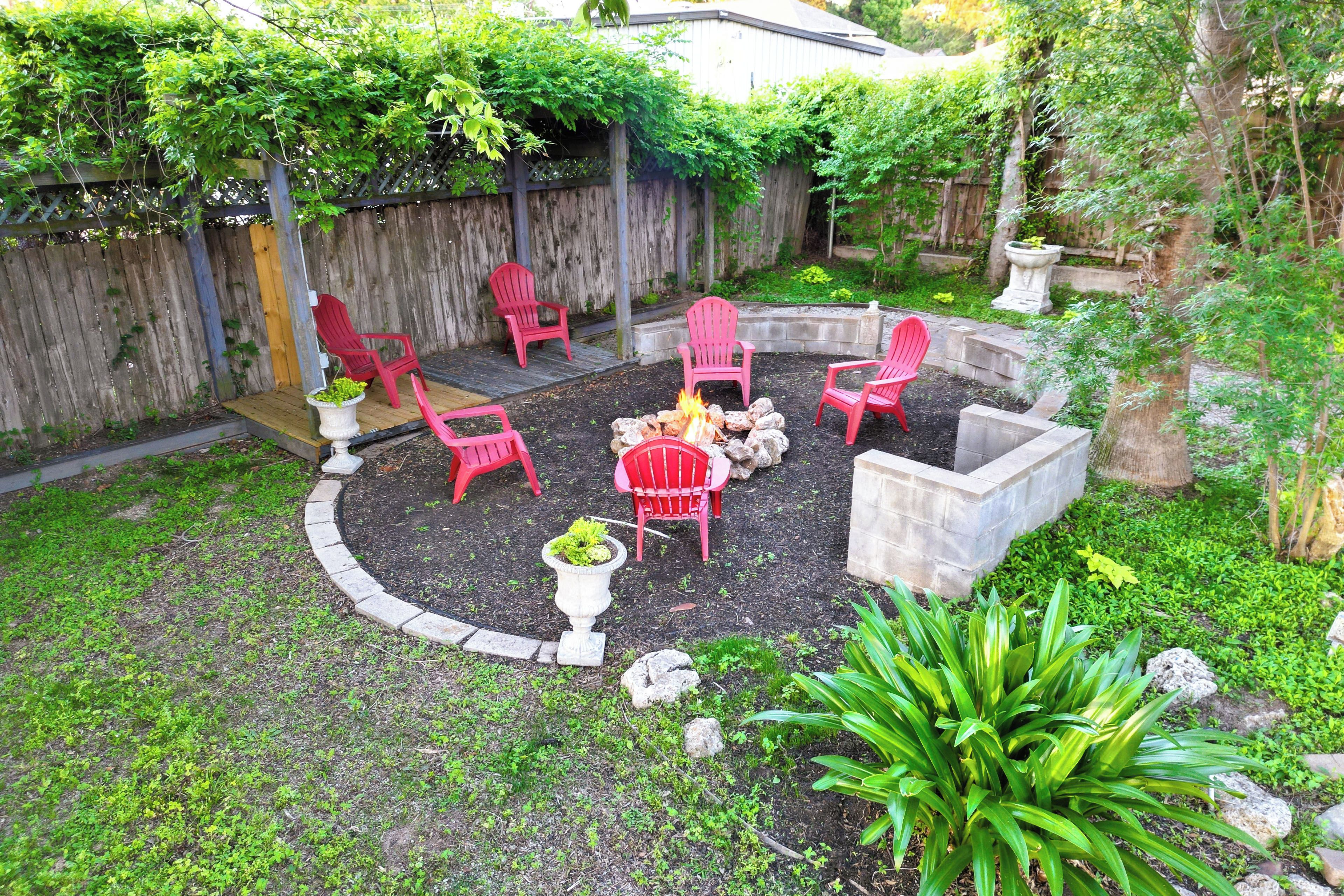 A backyard with a fire pit, red chairs, and a wooden deck.