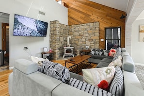 A modern living room with a stone wall, a fireplace, a large flat-screen TV, and a grey sectional sofa. - Group Getaway w/ Lake Views in Bronston! (Bronston)