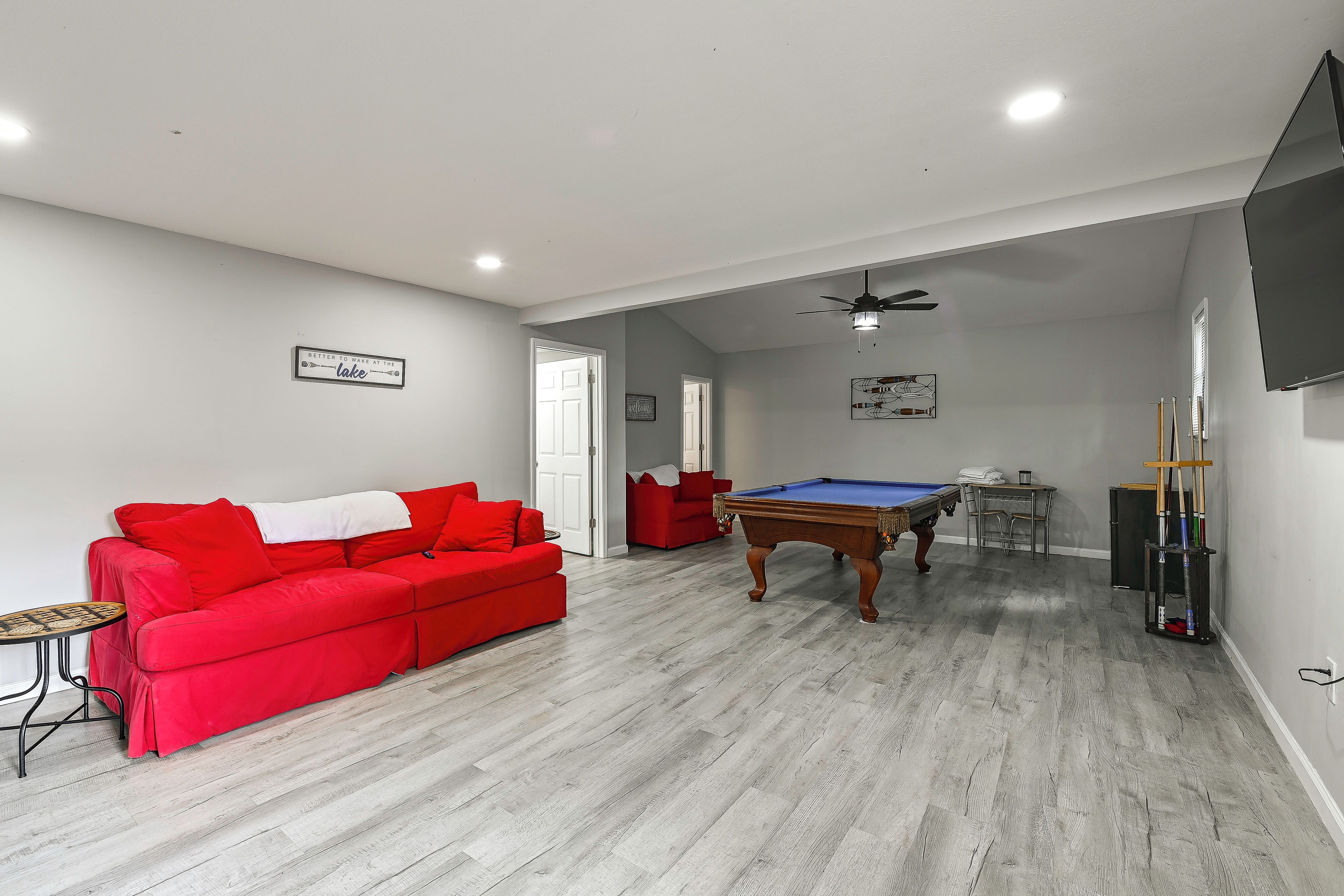 A living room with a red sofa, a pool table, and a ceiling fan.