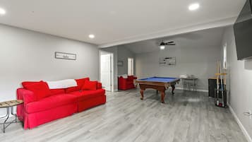 A living room with a red sofa, a pool table, and a ceiling fan.