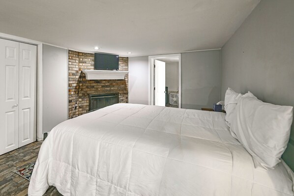 A bedroom with a brick fireplace, a bed with white bedding, and a door to the left. - Group Getaway w/ Lake Access in Bronston! (Bronston)