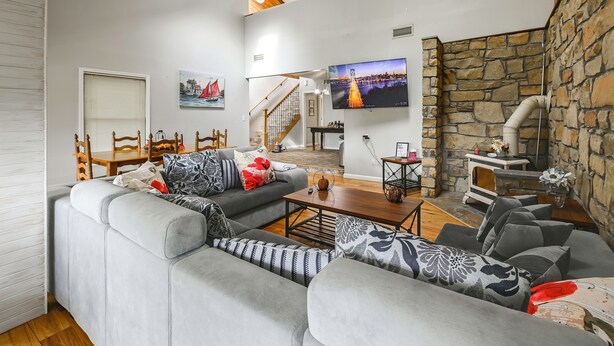 A modern living room with a sectional sofa, a wooden dining table, a fireplace, and a television mounted on the wall. - Group Getaway w/ Lake Views in Bronston! (Bronston)