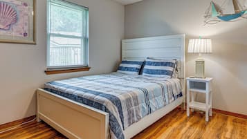 A bedroom with a bed, a nightstand, a lamp, a window with blinds, and a wall decoration.