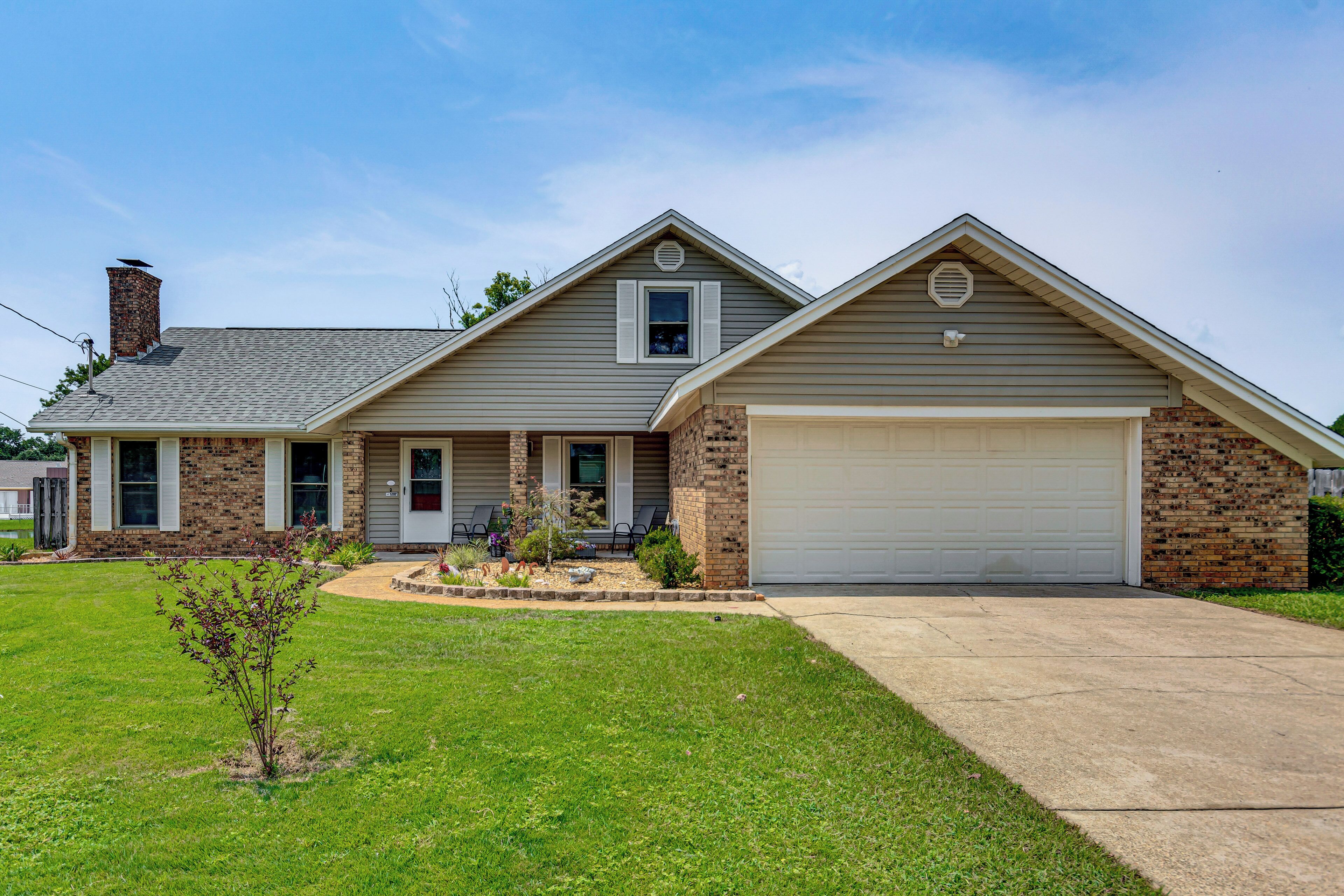 A two-story house with a garage, a brick chimney, and a well-maintained lawn.
