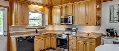 Una cocina con armarios de madera, lavavajillas, microondas, horno y cafetera.