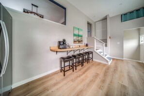 A modern kitchen with a built-in coffee machine, wooden bar stools, and a staircase leading to a loft area. - Family Fun! Indoor Jungle Gym, Hot Tub & Beach (Erie)