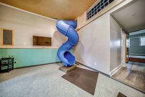 A spiral slide in a hallway with a wooden floor and a green wall. - Family Fun! Indoor Jungle Gym, Hot Tub & Beach (Erie)