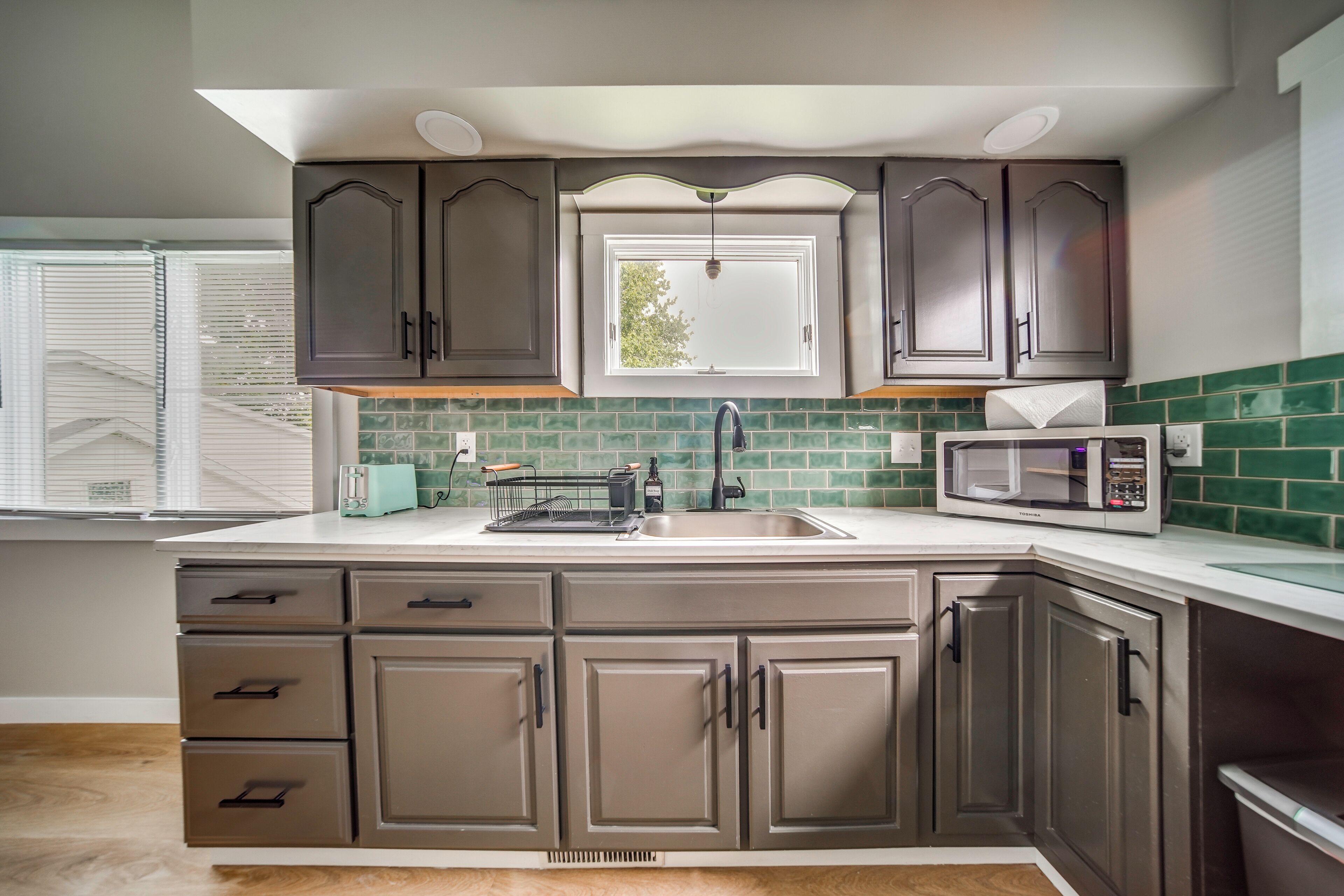 A kitchen with dark cabinets, a window, a microwave, and a toaster.
