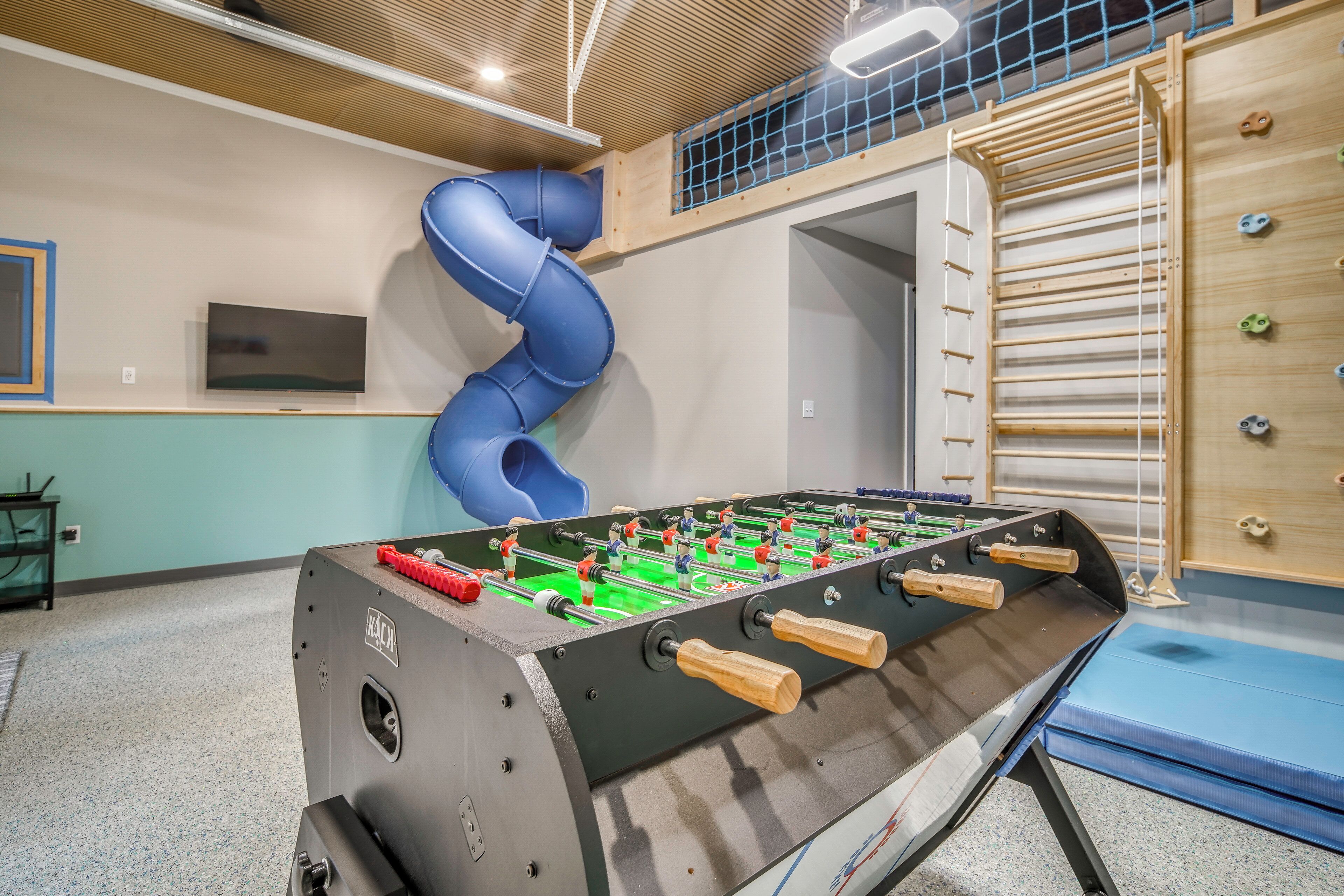 A foosball table in a room with a blue slide and climbing wall.