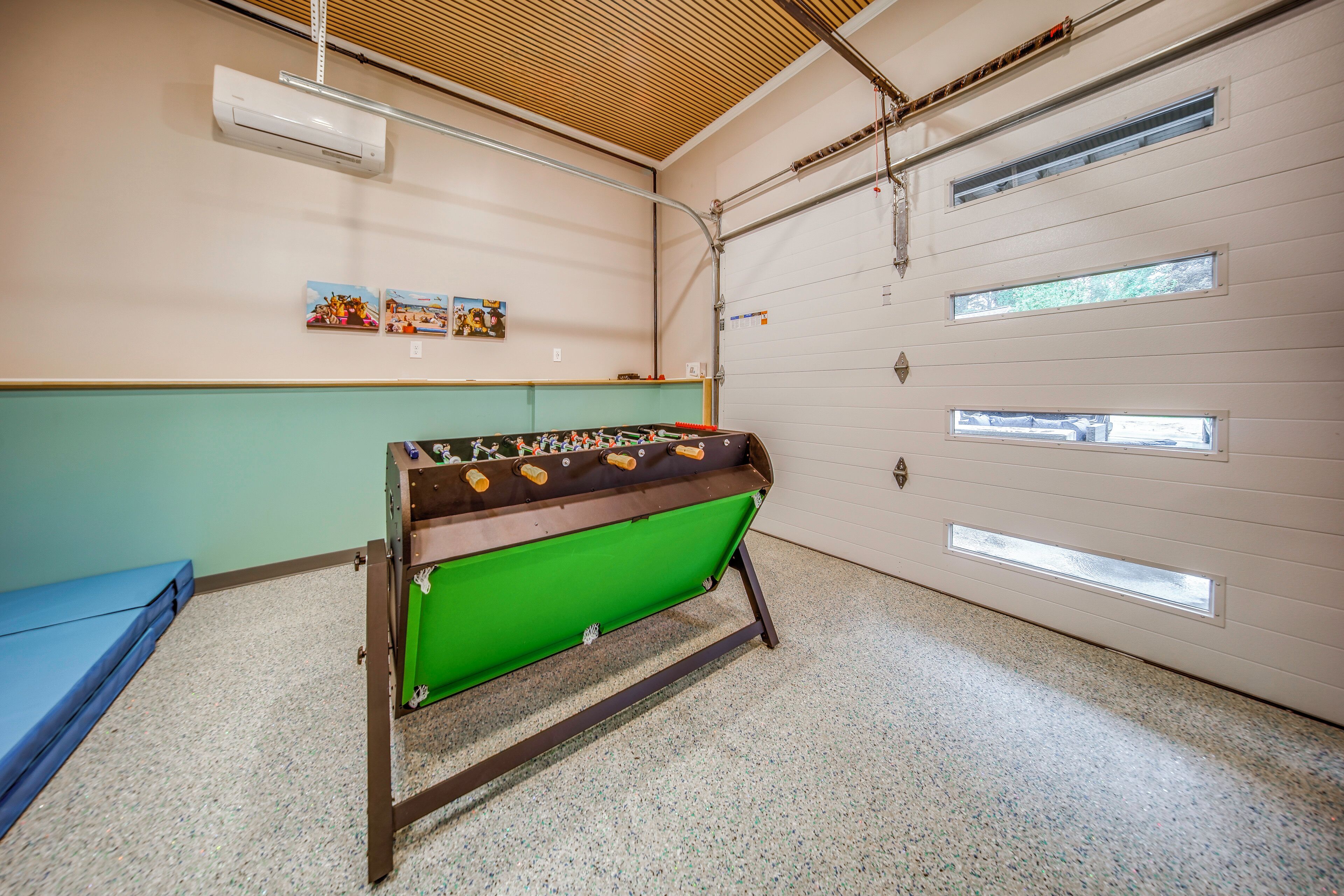 Una habitación con una mesa de fútbol verde, un sofá azul y una puerta blanca con amplias ventanas.
