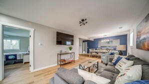 A modern living room with a grey sofa, a coffee table, and a dining area with chairs and a table. - Family Fun! Indoor Jungle Gym, Hot Tub & Beach (Erie)