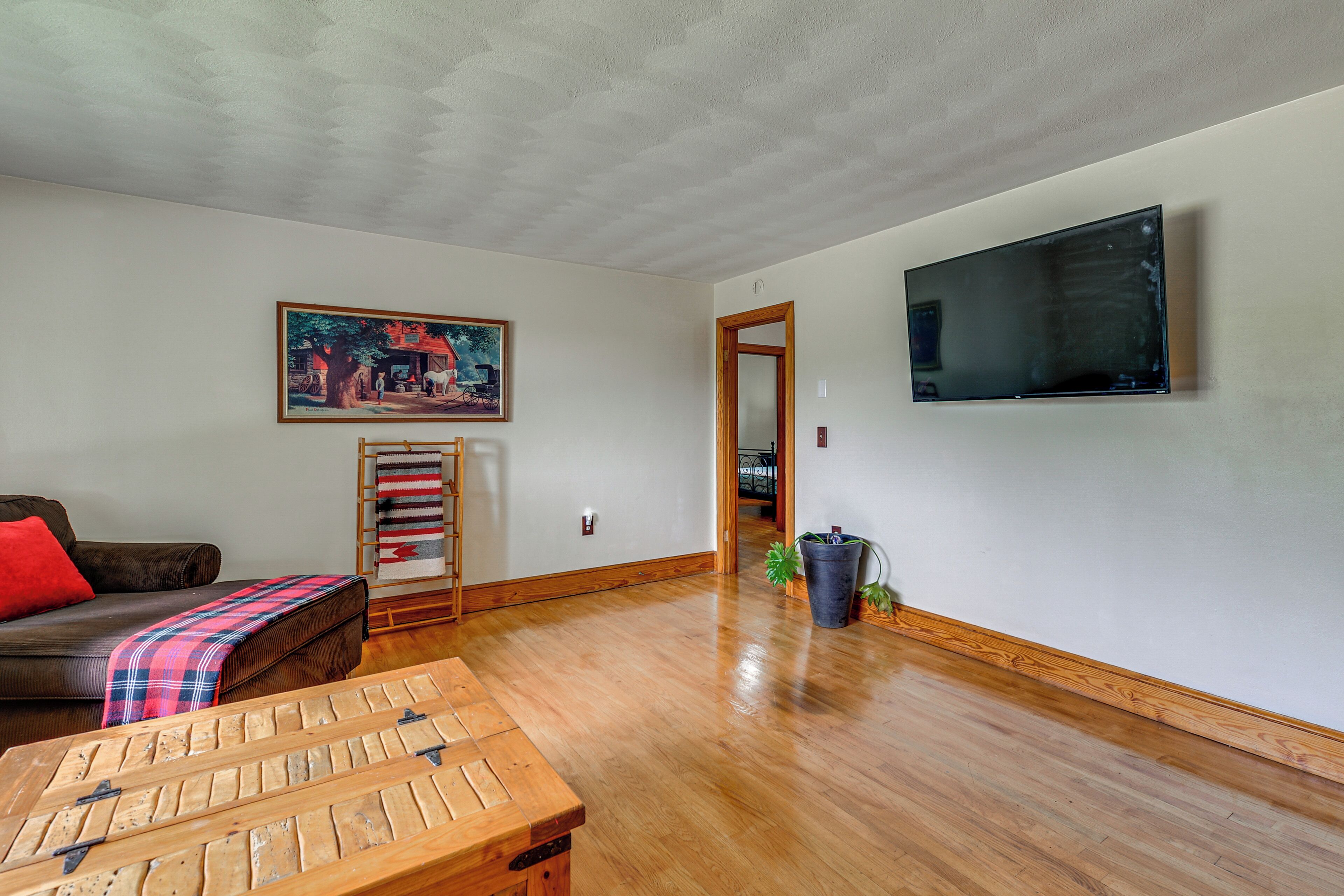 Una sala de estar con una mesa de centro de madera, un sofá, un cuadro, un televisor y una planta en maceta.