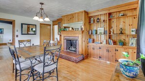 A dining area with a wooden table and chairs, a fireplace, and wooden shelving with various items. - Quiet Stuart Retreat w/ Yard & Fireplace (Patrick Springs)