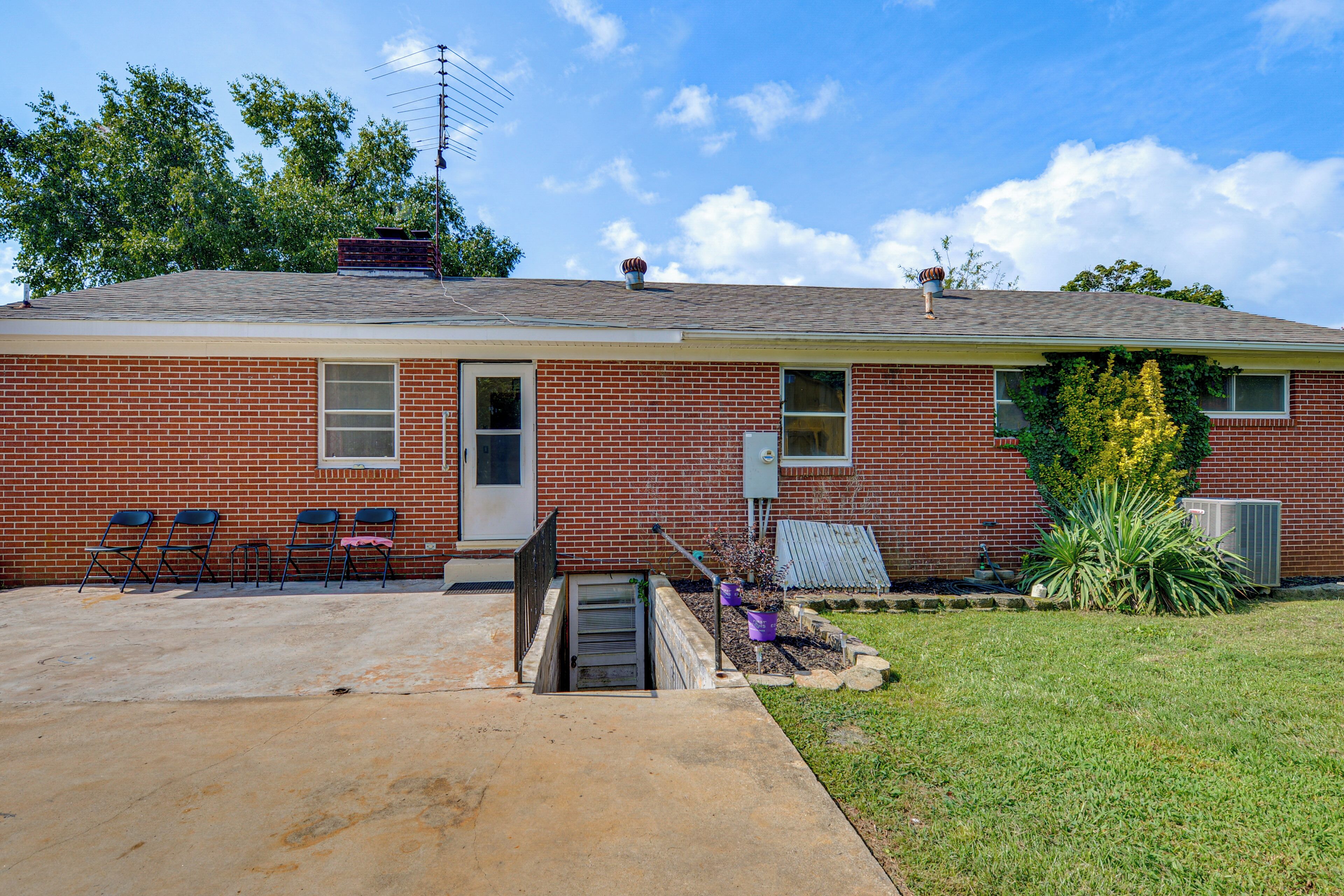 A single-story brick house with a front door, two windows, and a small porch with chairs.